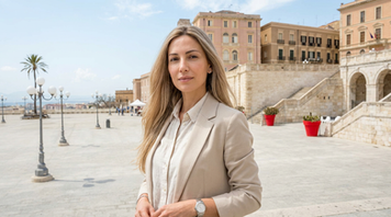 Donna italo‑mediorientale con capelli lunghi biondo sabbia/perla al Bastione di Saint Remy a Cagliari, terrazza panoramica sullo sfondo.