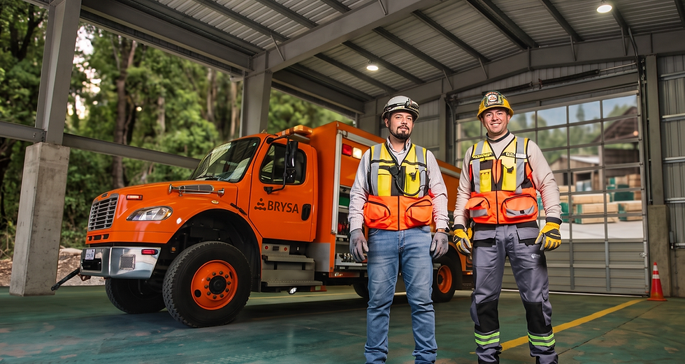 Dos trabajadores con casco y chaleco junto a un camión naranja BRYSA en un garaje, posan sonrientes.
