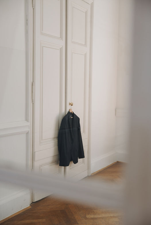 Black coat hanging on a wooden hanger on a white door in a room.