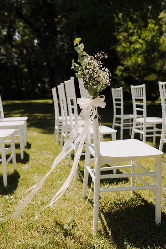 White chairs with floral decorations in a garden wedding setting. 