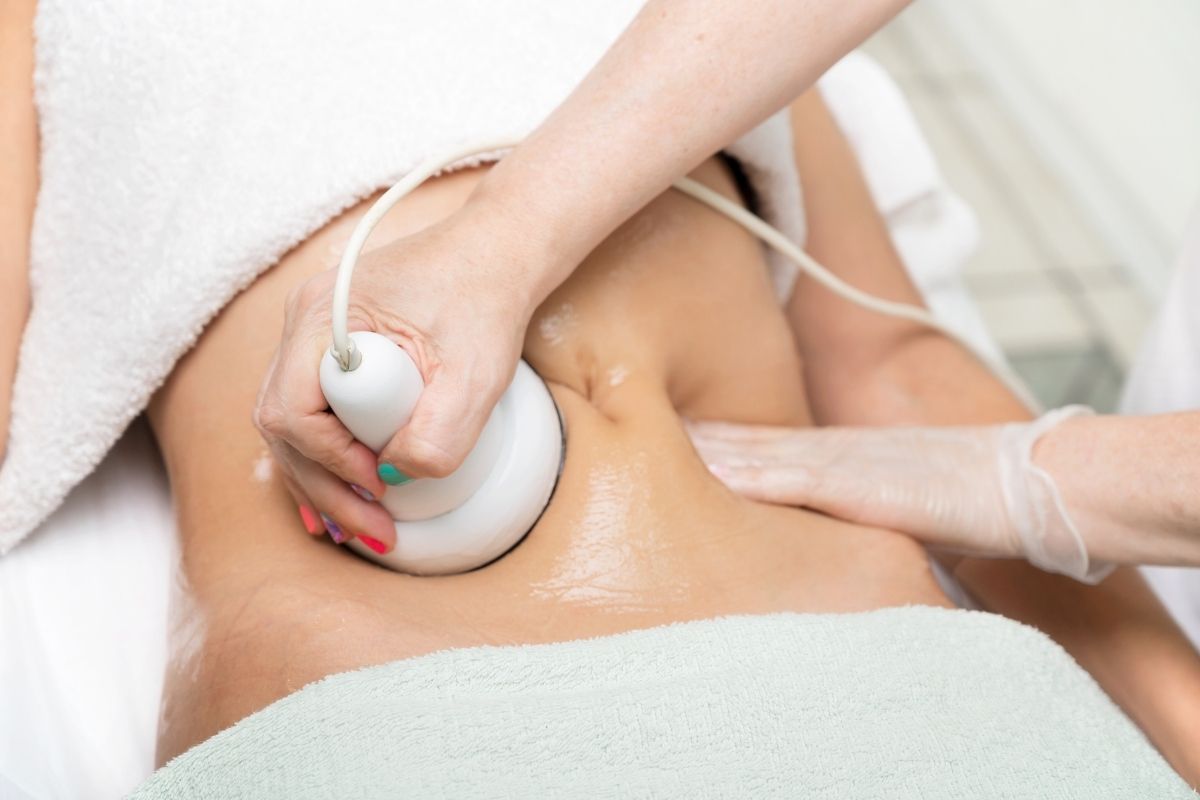 Technician performing ultrasound cavitation therapy for fat reduction.