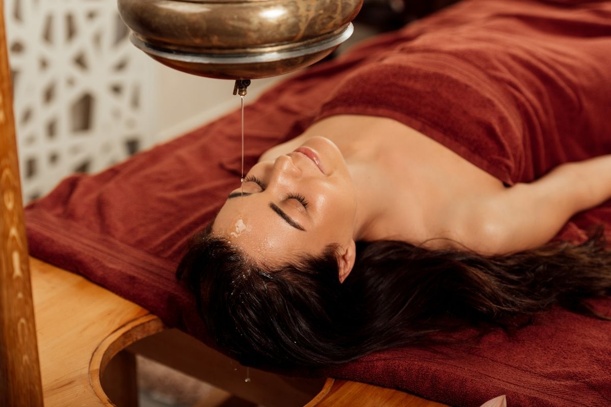An Ayurvedic therapist performing Shirodhara therapy, pouring warm oil onto the forehead for stress relief and relaxation.