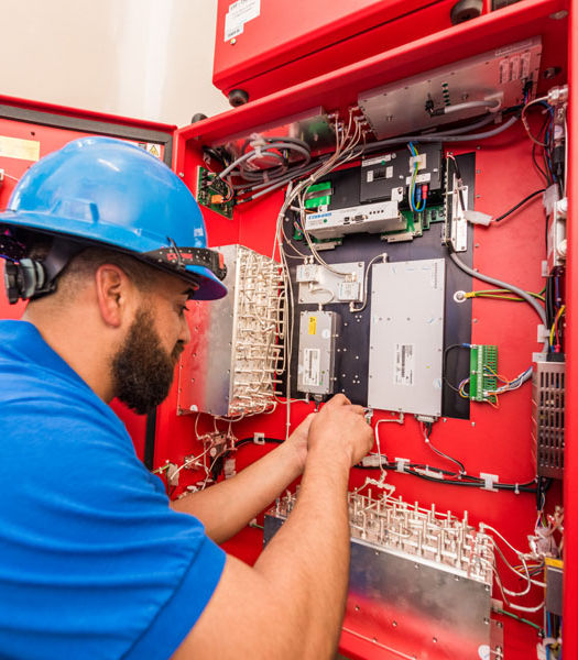 Technician in a hard hat inspecting a red electrical panel.