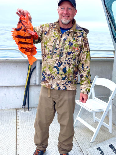 Jimmy standing on the dock of a boat holding about a 12" orange and black fish.