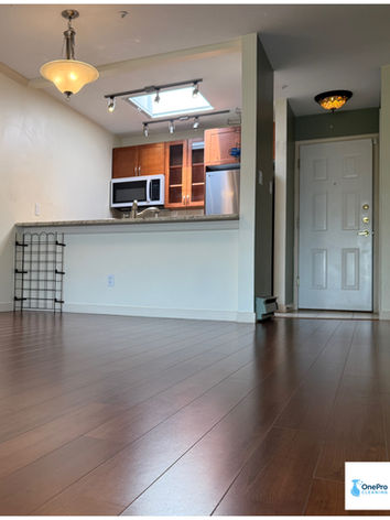 Dark polished hardwood floor in a bright living area facing a kitchen counter and entryway in Quayside.