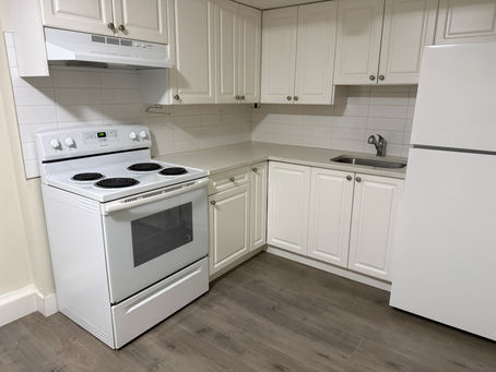 A completely sanitized and grease-free white kitchen inside a 2-bedroom basement suite, prepared for landlord inspection during a move-out cleaning in Surrey