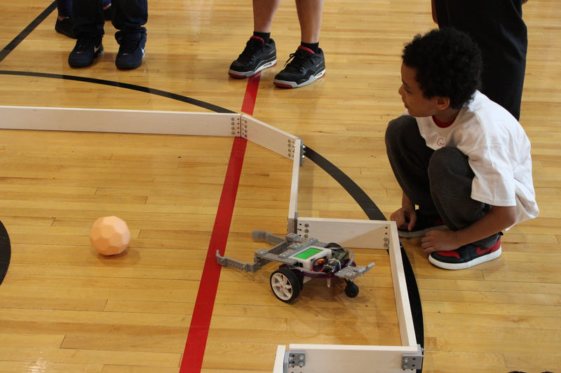 A student watches closely as a robot chases the ball.