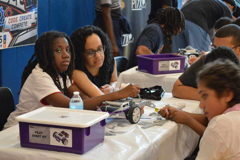 Students and a teacher work on a robot kit together.