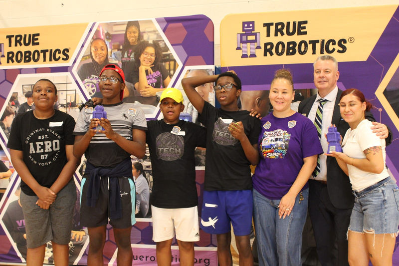 Students celebrate with their trophies at the True Robotics backdrop.