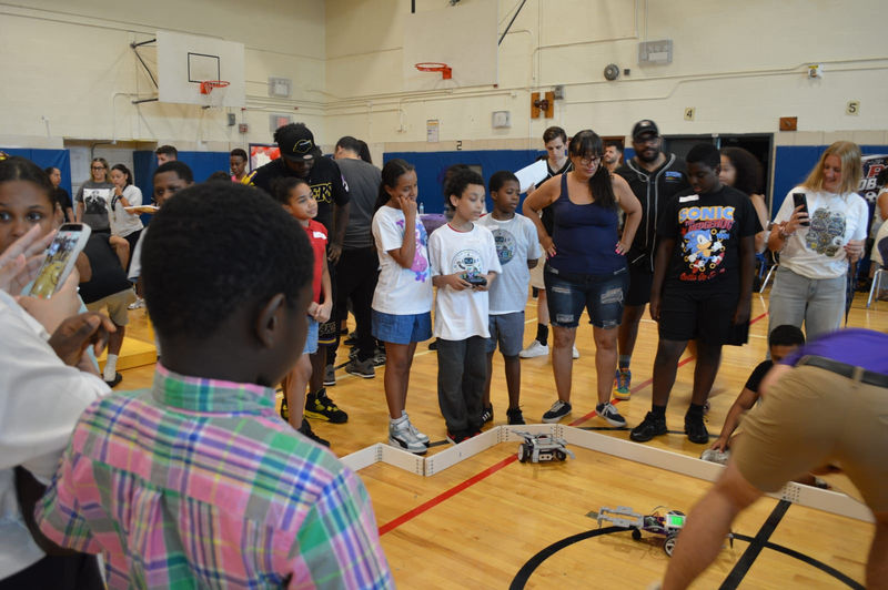A crowd of students and families surrounds the competition arena.