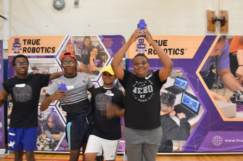 A team celebrates with the trophy at the True Robotics backdrop.