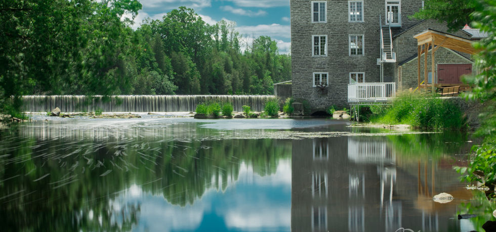 Spencerville Mill reflected in calm water - fine art photograph of a winding country road lined with vibrant autumn foliage, available as fine art prints and photo gifts through AMayesZing Photography Co.
