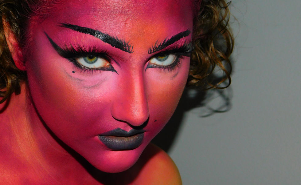 Image containing female monster, glaring up at the camera. High contrast red and orange painted skin and bright highlights, "angry" black brows and age lines, sharp and thick eyeliner, and a bold black with sharp cupid's bow. 