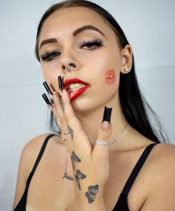 Image containing close up shot of female, looking into the camera, with thick lashes, dark brows, red lips, and red kiss on cheeks