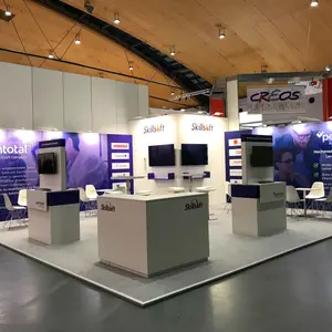 Изложбен щанд на Skillsoft на изложение в Карлсруе, представящ платформи за дигитално обучение SumTotal и Percipio. Щандът е с отворена структура, с няколко обособени зони за разговори, брандирани рецепции и стени с информационна графика. Включени са четири екрана, монтирани на вертикални панели и стени, използвани за видео съдържание и демонстрации. Дизайнът е изчистен и подчертано корпоративен, с доминиращи цветове бяло, лилаво и сиво. Щандът комуникира модерни HR и e-learning решения за корпоративния сектор.