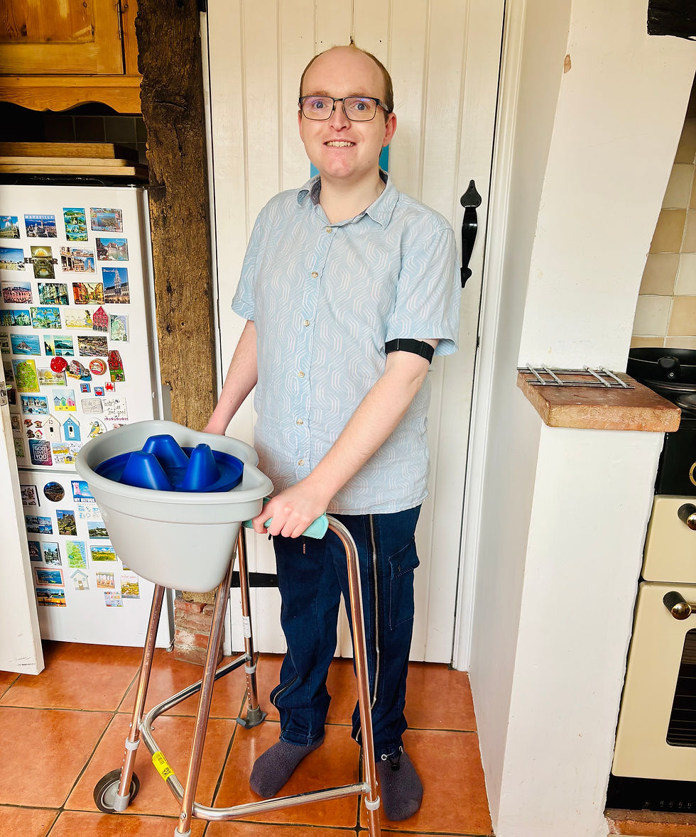 In a kitchen, a man wearing denim cargo trousers stands with a walker for assistance.