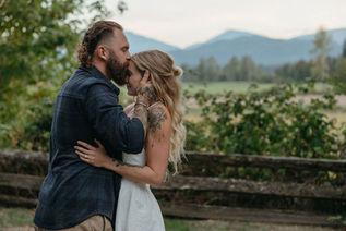 Couple embraced in from of a fenced field, man kissing female's forehead with hands cupping face. Engagement shoot package with makeup and hair by Candice Deanna at Empress Acres Nanaimo Vancouver Island.