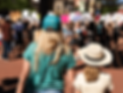 A woman and young girl in hats with their backs to the camera fill the foreground as a crowd of protestors fills the background in soft-focus
