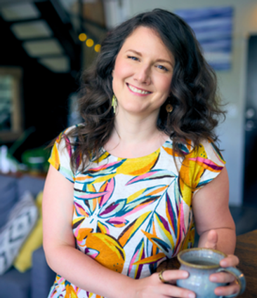 Justine Ramdas smiling in floral blouse holding a ceramic mug of tea