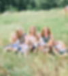 A cluster of three moms and six children cuddle in a field of tall green grass looking around and laughing