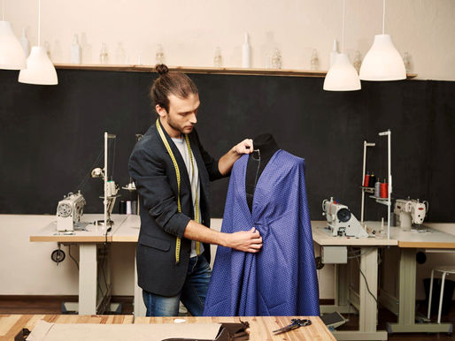 A designer meticulously evaluates a vibrant blue garment on a dress form in a modern workshop, surrounded by sewing machines and tools, showcasing his dedication to craftsmanship.
