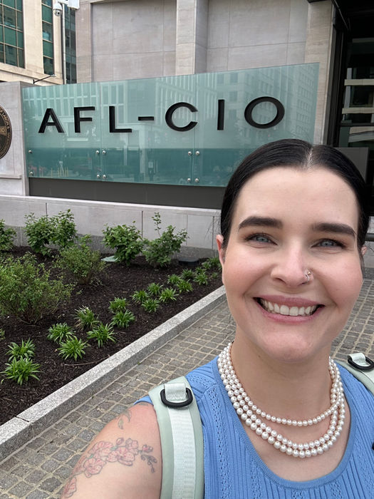 Smiling woman in front of AFL-CIO sign. Blythe Potter MEDIA. Building in background.