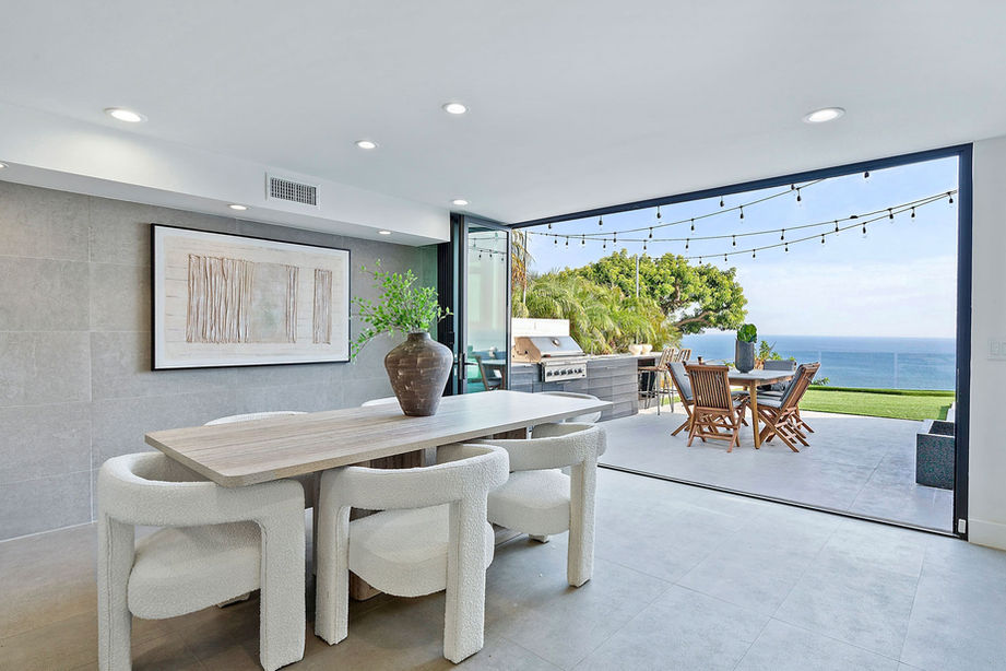 Exterior shot of a luxury villa featuring large glass sliding doors, a swimming pool, and outdoor lounge furniture.