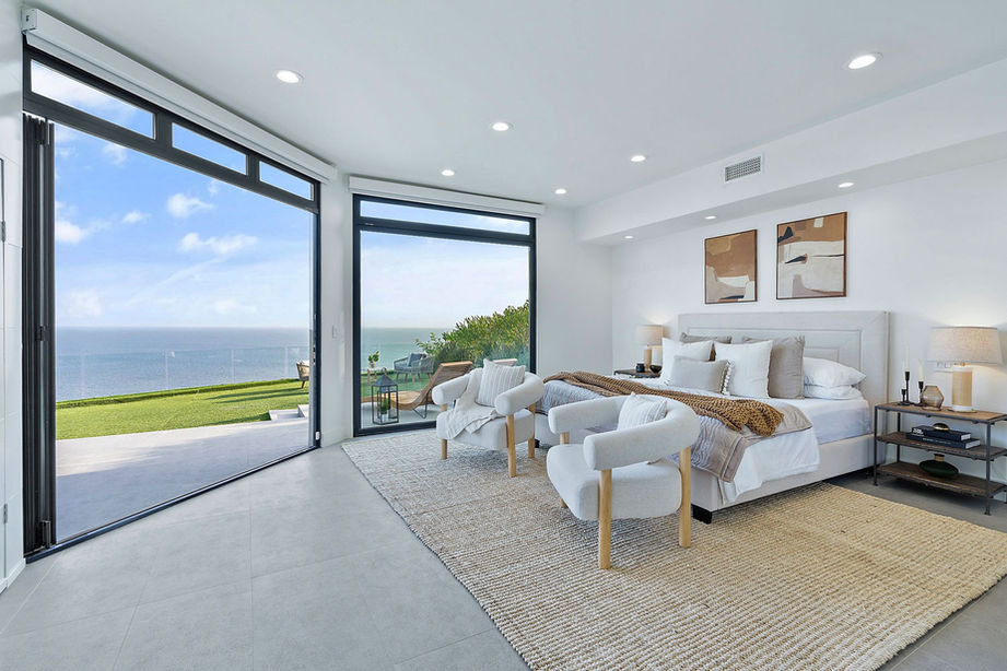 Exterior shot of a luxury villa featuring large glass sliding doors, a swimming pool, and outdoor lounge furniture.
