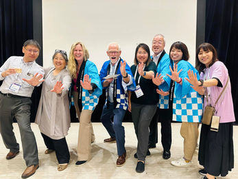 This joyful photo captures a group of international IEEE members and volunteers striking a fun pose together at a conference or social event. Dressed in a mix of traditional Japanese happi coats and casual attire, the group radiates camaraderie, energy, and cross-cultural friendship—highlighting the spirit of global collaboration in the IEEE community.