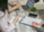 People discuss a home insurance policy at a rustic table with laptop, notebook, phone, and plant in a focused meeting.