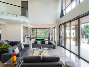 Bright modern living room with gray sofas, a pool table, glass balcony, and large windows opening to a patio and pool.