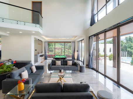 Bright modern living room with gray sofas, a pool table, glass balcony, and large windows opening to a patio and pool.