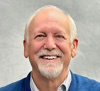 Professional profile of Dr. Kevin Downing with a beige background, a white shirt, blue sweater, and a big smile.
