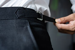 A man's hand is holding the edge of an elastic belt. Black trousers for men that can be st