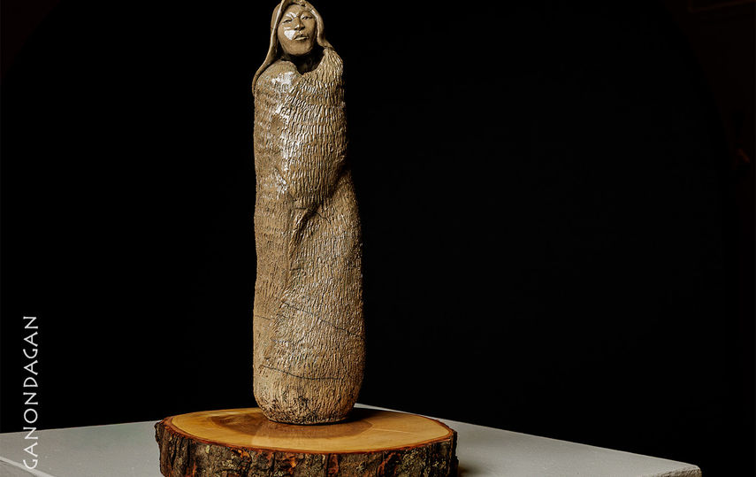sculpture of a woman a blanket wrapped around her shoulders with wooden base