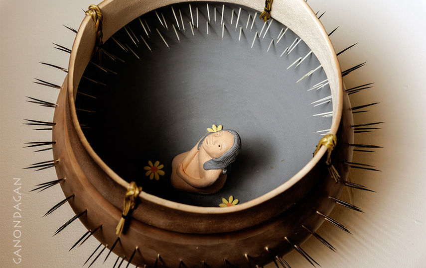 a little girl kneeling inside a pot that is pierced through with spikes