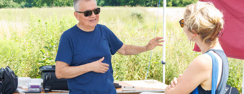A man in a vending tent with jewelry displays talks to a customer