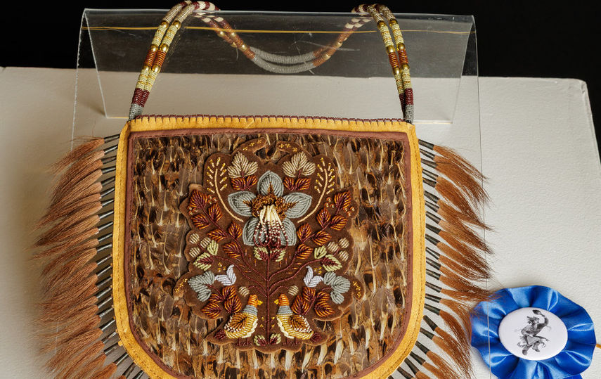 beaded and tufted purse with blue ribbon next to it