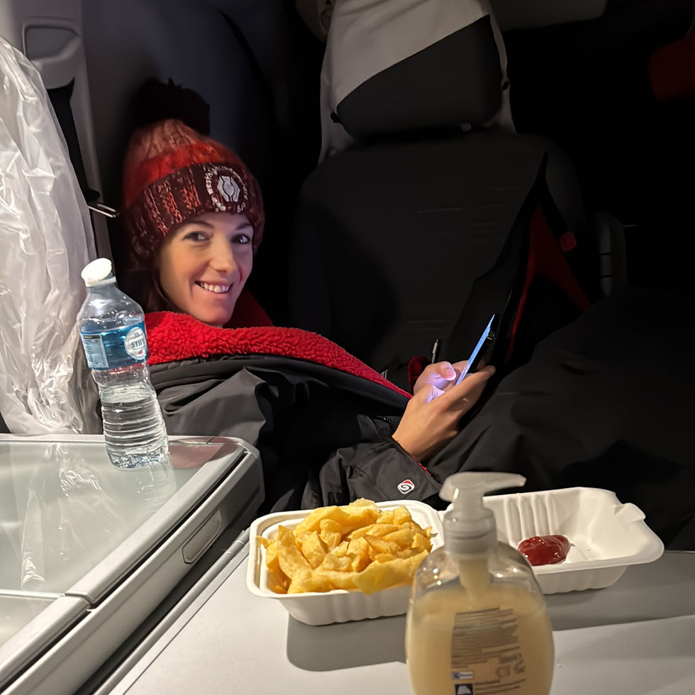 Smiling person in red hat uses phone in car, with fries, ketchup, and water on table. Cozy, relaxed setting, dim lighting.