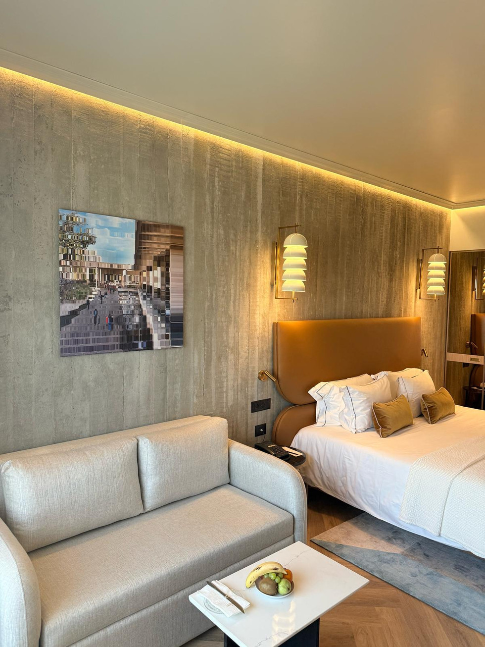 Modern hotel room with bed, sofa, artwork, and stone wall. 