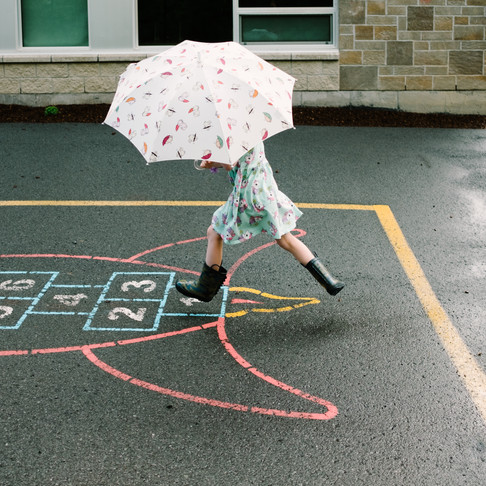 Girl with umbrella jumping in school yard. Family photography session.