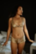 Woman standing facing forward wearing a matching silk nude bralette and silk nude shorties.