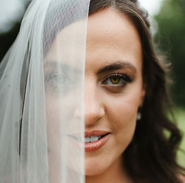 ALT="Close-up portrait of a bride with a veil covering the left side of her face, revealing her right eye, nose, and mouth"