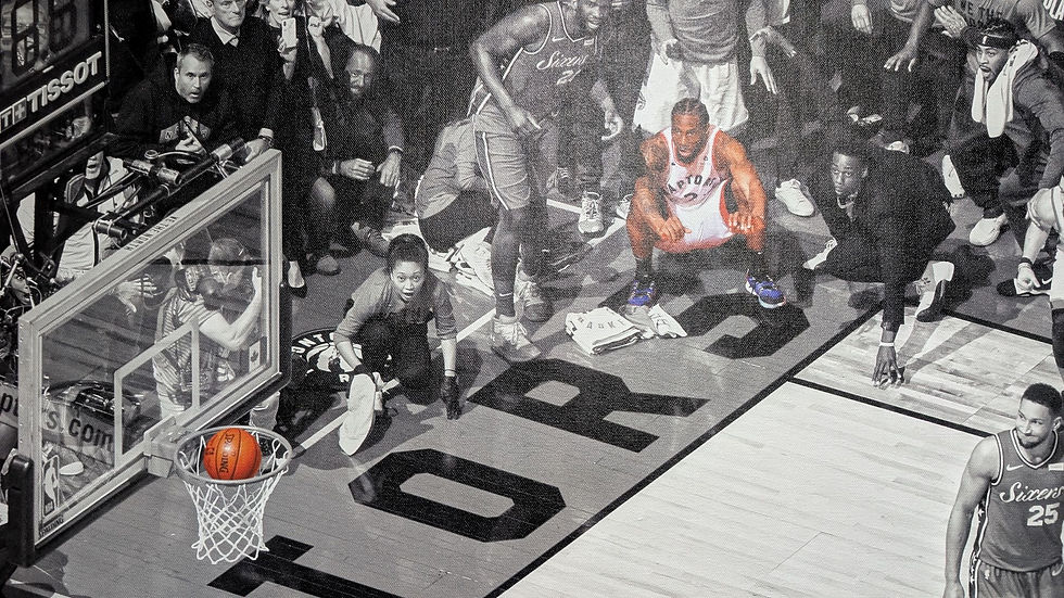 Kawhi Leonard, crouching, focused as a ball nears the hoop. Crowd in background, some players in jerseys. Intense, anticipatory mood.