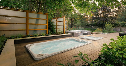 A hot tub and swim spa installed in decking, the garden surround is green and flourishing.