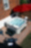 An aerial view of the blue sparkling clean water of a Hydropool Signature Hot Tub seen next to a spread of snacks underneath a red umbrella..