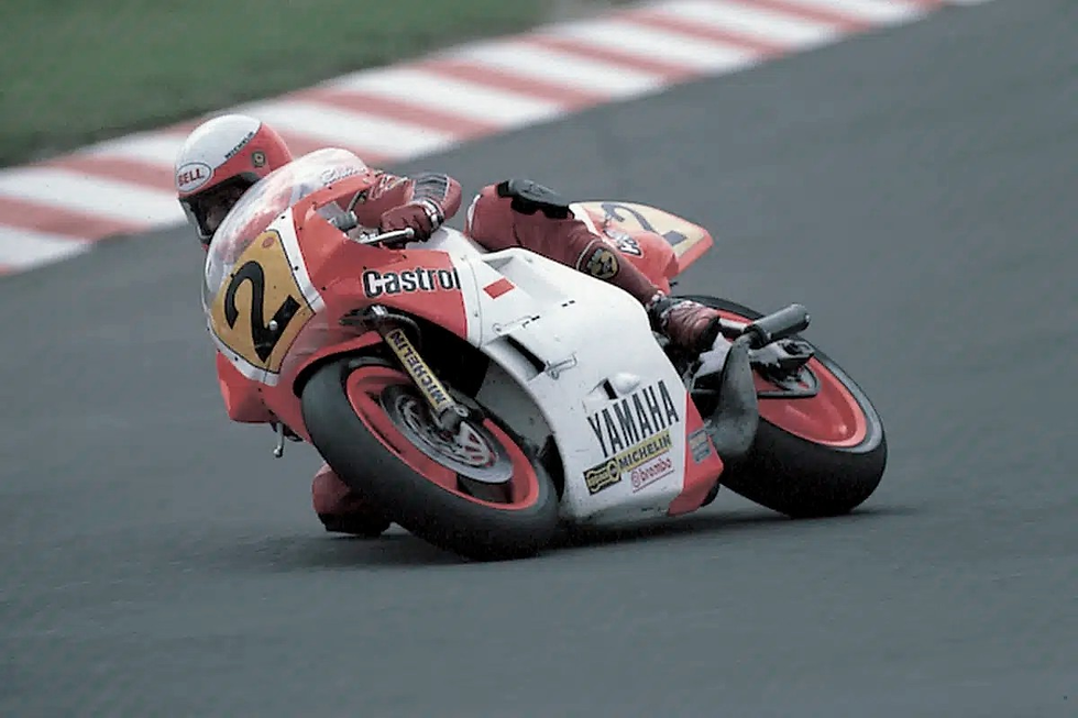 Rider in red gear leans into a sharp turn on a red-and-white Yamaha motorcycle. Visible logos: Castrol, Michelin. Track background.
