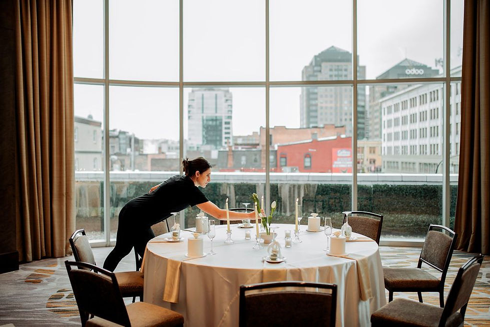 Woman setting a round dining table in an elegant room with large windows and a city skyline in the background. The Westin, wny wedding venues, buffalo weddings