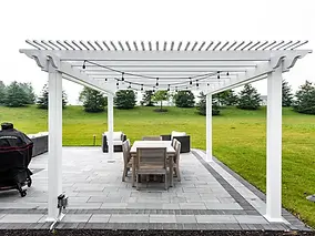 White pergola over a stone patio with outdoor dining set.