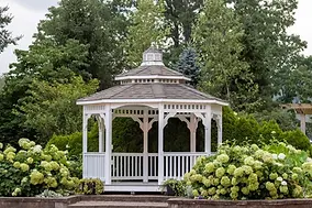 White octagonal gazebo surrounded by green shrubs and trees